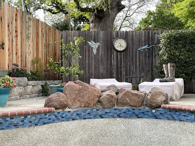 A backyard with a pool, rocks and a clock